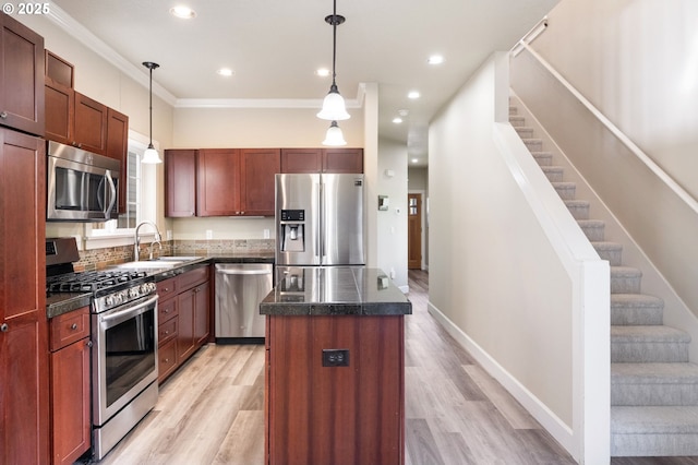 kitchen featuring appliances with stainless steel finishes, a sink, a center island, light wood-style floors, and pendant lighting