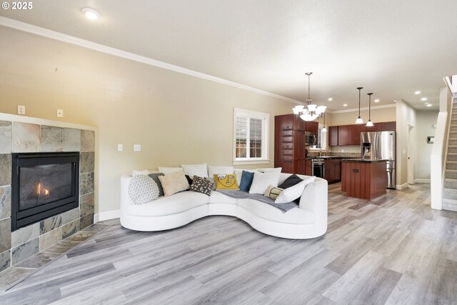 living area featuring stairs, light wood-style floors, baseboards, a tile fireplace, and crown molding