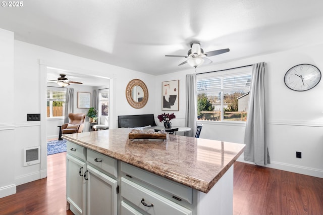 kitchen featuring dark wood-type flooring, light stone countertops, ceiling fan, and a kitchen island