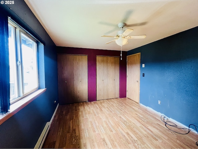 unfurnished bedroom featuring a ceiling fan, baseboards, two closets, and wood finished floors