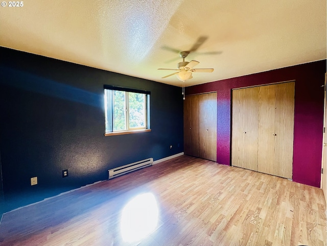 unfurnished bedroom featuring multiple closets, a baseboard heating unit, ceiling fan, a textured ceiling, and wood finished floors