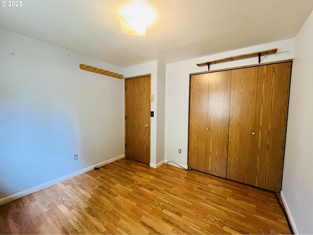 unfurnished bedroom with a closet, a textured ceiling, baseboards, and wood finished floors