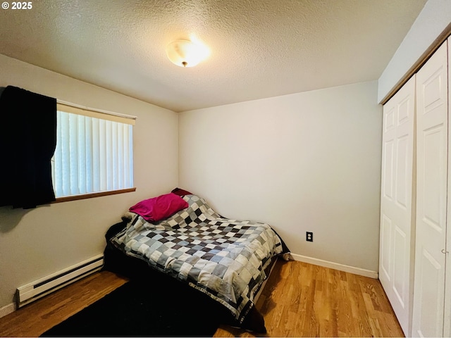 bedroom featuring baseboards, wood finished floors, baseboard heating, a textured ceiling, and a closet