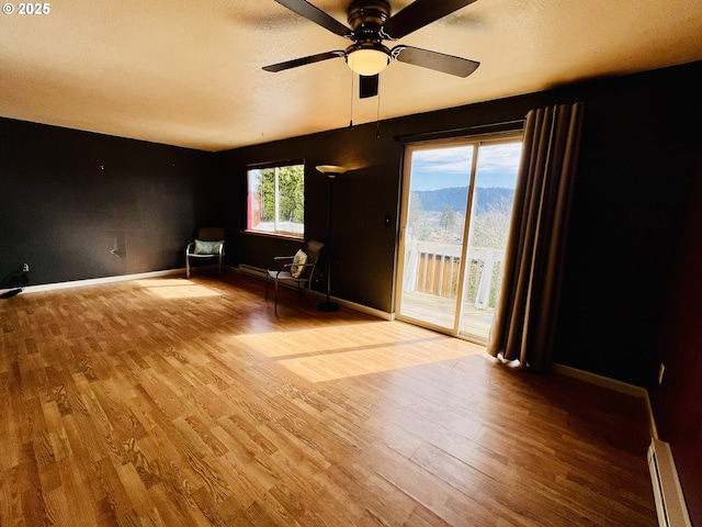 unfurnished room featuring a baseboard heating unit, ceiling fan, wood finished floors, and baseboards