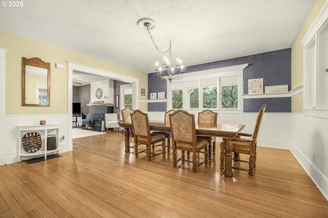 dining area featuring light wood-type flooring, an inviting chandelier, a fireplace, and wainscoting