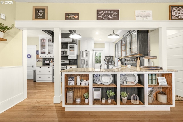 interior space with appliances with stainless steel finishes, pendant lighting, wainscoting, and light wood-style floors