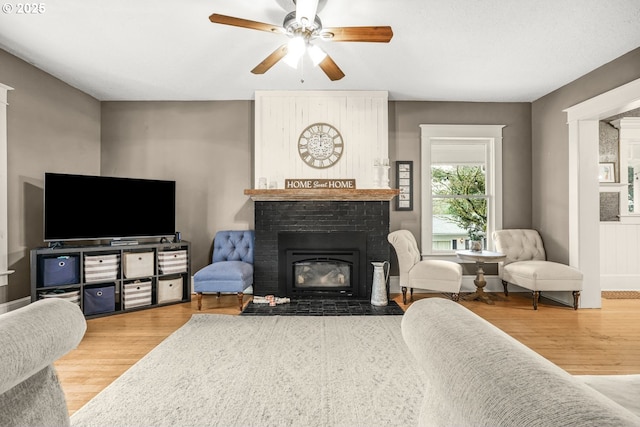 living room featuring a brick fireplace, a ceiling fan, and wood finished floors