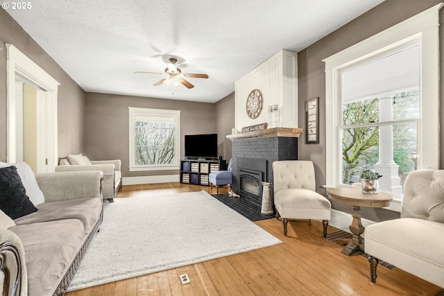 living room featuring light wood finished floors, plenty of natural light, ceiling fan, and a textured ceiling