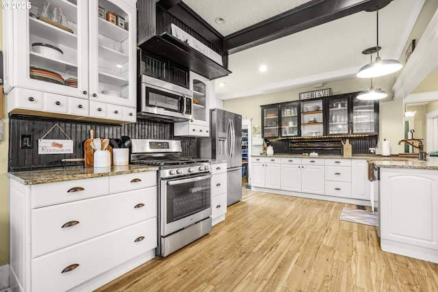 kitchen featuring light stone counters, stainless steel appliances, glass insert cabinets, light wood-style floors, and white cabinets