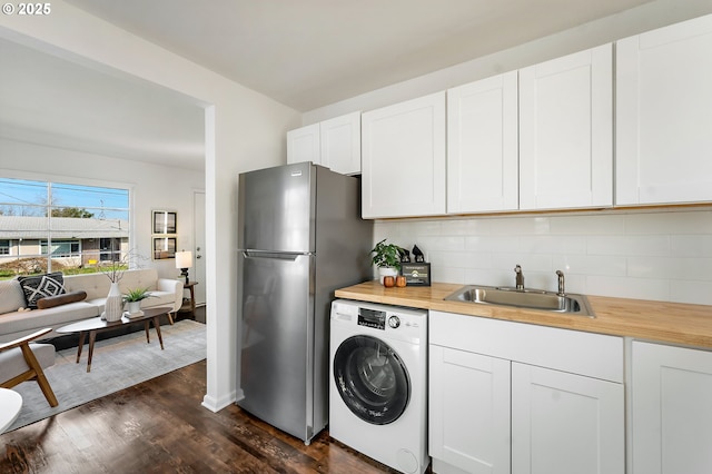 kitchen featuring butcher block countertops, dark wood-type flooring, a sink, freestanding refrigerator, and washer / dryer