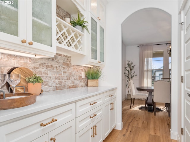 bar featuring decorative backsplash, light hardwood / wood-style floors, and white cabinets