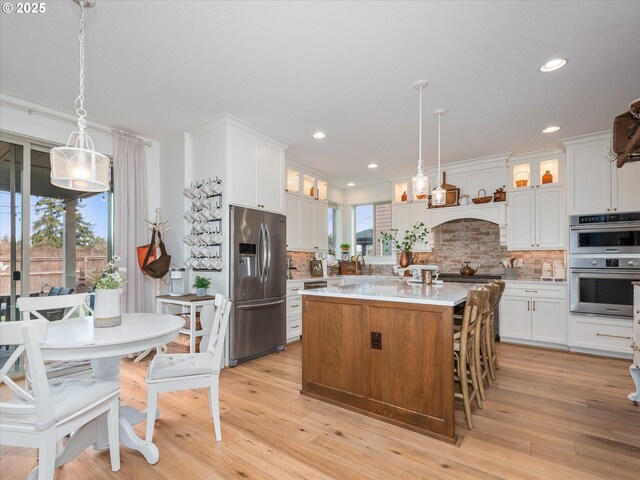 kitchen with a kitchen island, appliances with stainless steel finishes, pendant lighting, and white cabinets