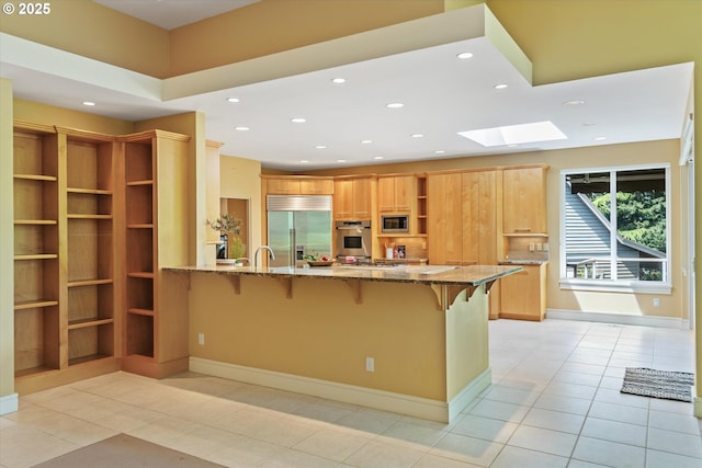 kitchen featuring built in appliances, a skylight, open shelves, light tile patterned floors, and a kitchen bar