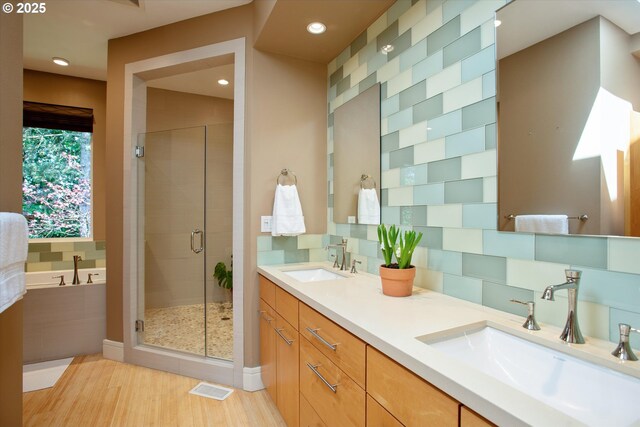 full bathroom featuring a stall shower, recessed lighting, a garden tub, wood finished floors, and double vanity