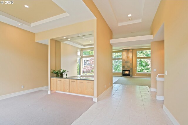 corridor featuring a raised ceiling, light colored carpet, healthy amount of natural light, and recessed lighting