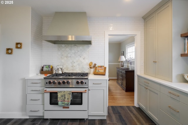 kitchen featuring high end stove, wall chimney exhaust hood, light countertops, decorative backsplash, and dark wood-style flooring