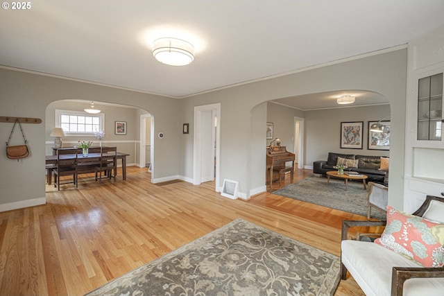 living area featuring visible vents, baseboards, light wood-style flooring, arched walkways, and ornamental molding