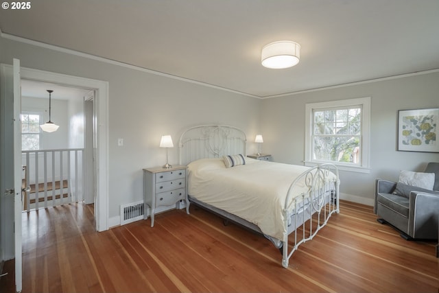 bedroom with crown molding, multiple windows, wood finished floors, and visible vents