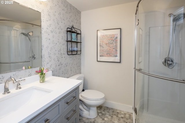 bathroom with a shower stall, wallpapered walls, baseboards, toilet, and vanity