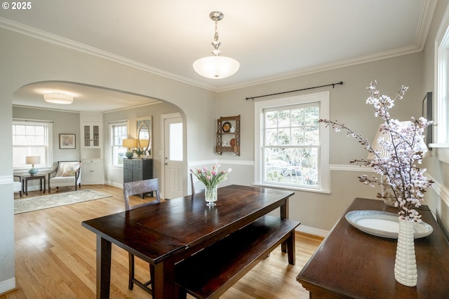 dining space with arched walkways, light wood-style flooring, baseboards, and ornamental molding