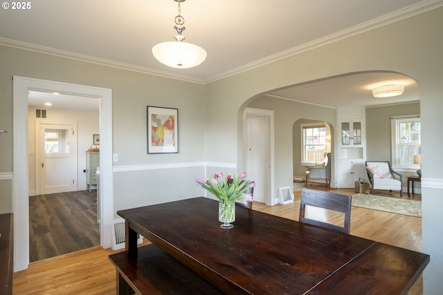 dining space with wood finished floors, crown molding, visible vents, and arched walkways