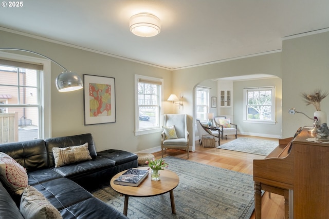 living area featuring arched walkways, crown molding, baseboards, and wood finished floors