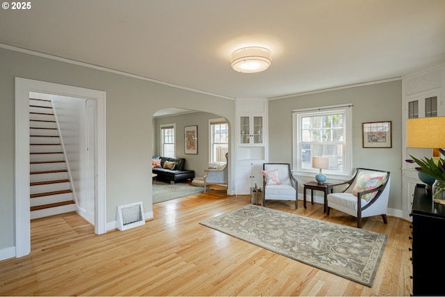 sitting room featuring visible vents, ornamental molding, arched walkways, light wood finished floors, and stairs