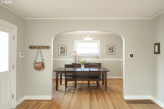 dining room featuring baseboards, arched walkways, crown molding, and light wood finished floors