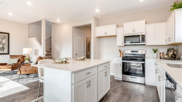 kitchen with dark wood-style floors, appliances with stainless steel finishes, a kitchen breakfast bar, light countertops, and white cabinetry