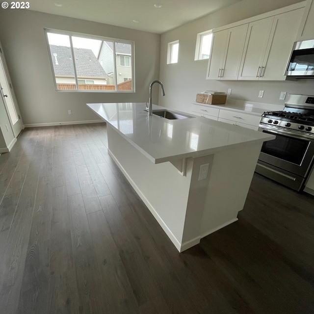kitchen featuring a sink, light countertops, dark wood finished floors, stainless steel appliances, and a center island with sink
