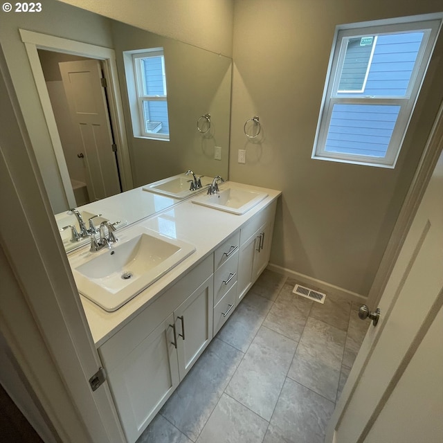 full bath with double vanity, baseboards, visible vents, and a sink