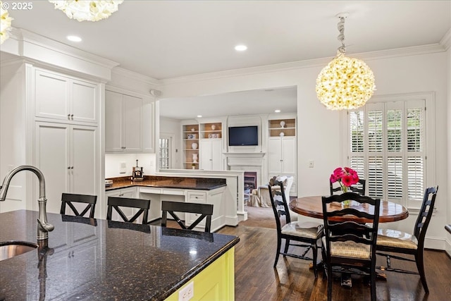 dining room featuring a chandelier, dark wood-style flooring, a fireplace, and ornamental molding