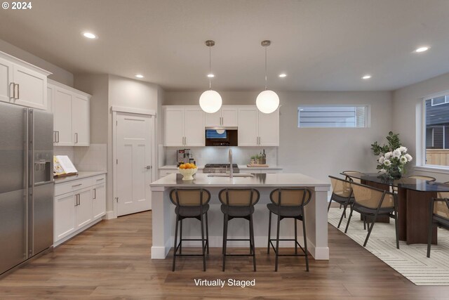 kitchen with stainless steel gas range, hanging light fixtures, light wood-type flooring, an island with sink, and white cabinets