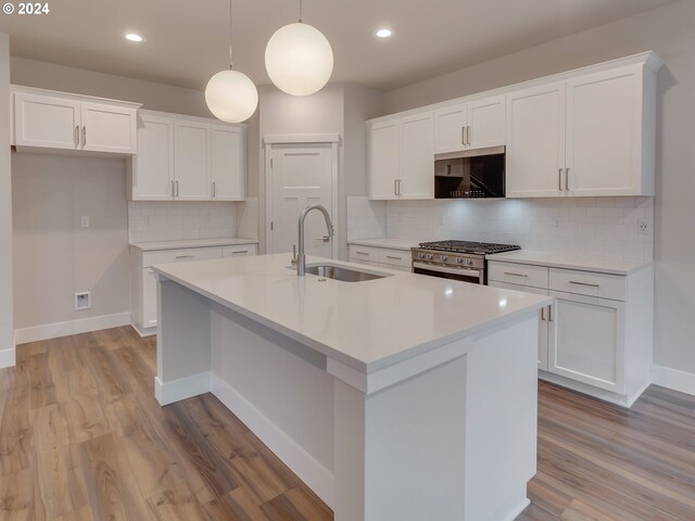 kitchen featuring stainless steel range with gas cooktop, decorative light fixtures, white cabinetry, sink, and a center island with sink