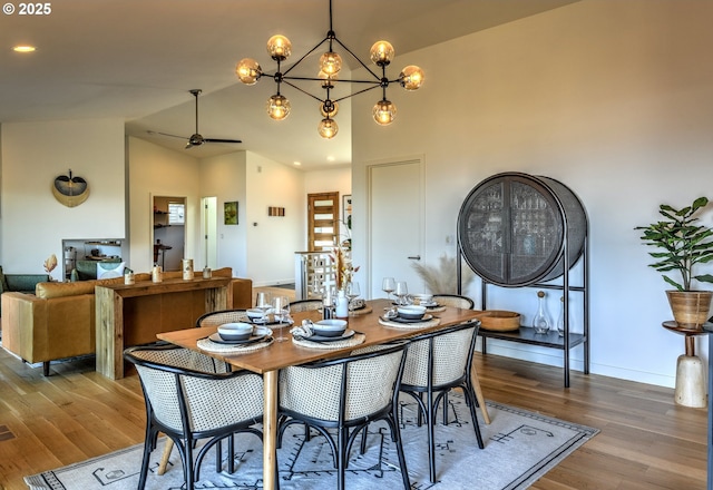 dining area featuring vaulted ceiling, ceiling fan with notable chandelier, wood finished floors, and baseboards