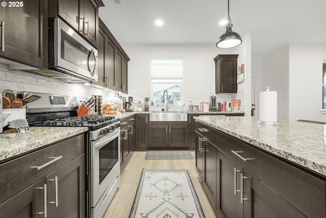 kitchen featuring light stone countertops, decorative light fixtures, decorative backsplash, appliances with stainless steel finishes, and sink