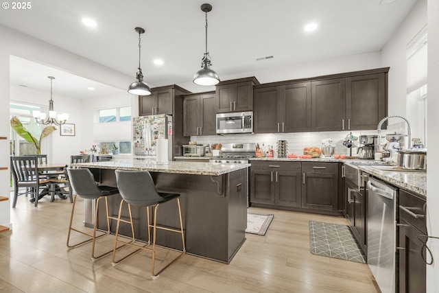 kitchen featuring light stone countertops, a kitchen island, an inviting chandelier, and appliances with stainless steel finishes