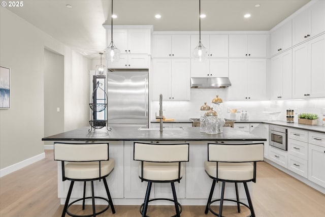 15007 Twin Fir Rd, Lake Oswego, OR 97035 - kitchen with appliances with stainless steel finishes, under cabinet range hood, dark countertops, white cabinets, and a center island with sink