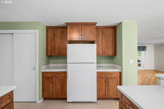 3985 Donald St, Eugene, OR 97405 - kitchen with freestanding refrigerator, brown cabinetry, a textured ceiling, and tile counters