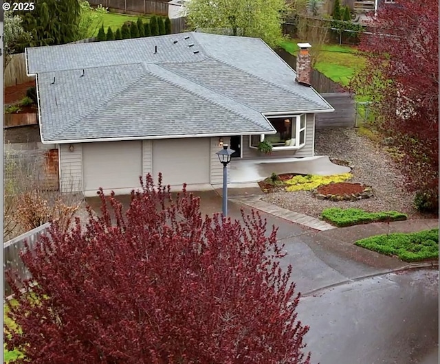 exterior space with an attached garage, fence, a shingled roof, and a chimney