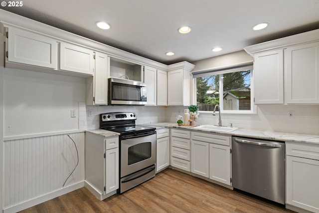 kitchen with wood finished floors, light stone countertops, white cabinets, a sink, and appliances with stainless steel finishes