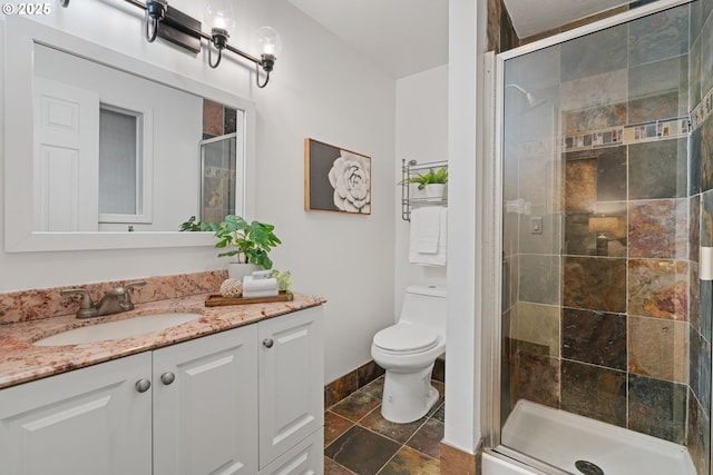 bathroom with stone finish flooring, a shower stall, vanity, baseboards, and toilet