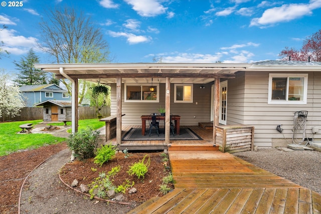 back of property with an outdoor structure, fence, a deck, outdoor dining area, and a storage unit