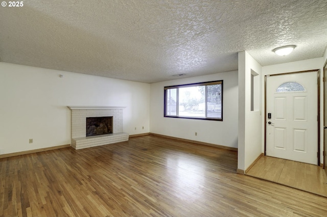 4805 NE 122nd Ave, Vancouver, WA 98682 - unfurnished living room featuring light wood finished floors, a textured ceiling, a brick fireplace, and baseboards
