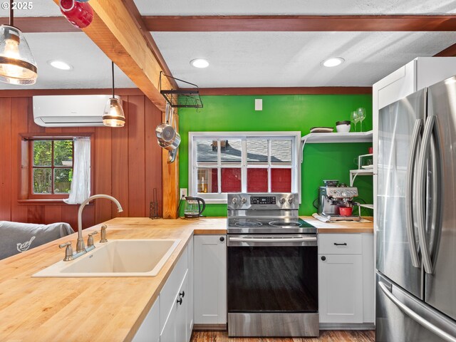 kitchen featuring a wall mounted AC, a sink, wood counters, stainless steel appliances, and white cabinetry