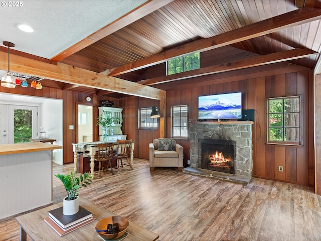living area featuring wooden walls, a stone fireplace, beam ceiling, and plenty of natural light
