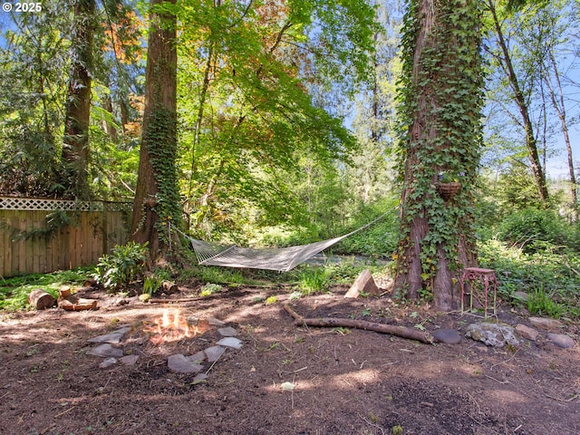 view of yard featuring a view of trees, a fire pit, and fence