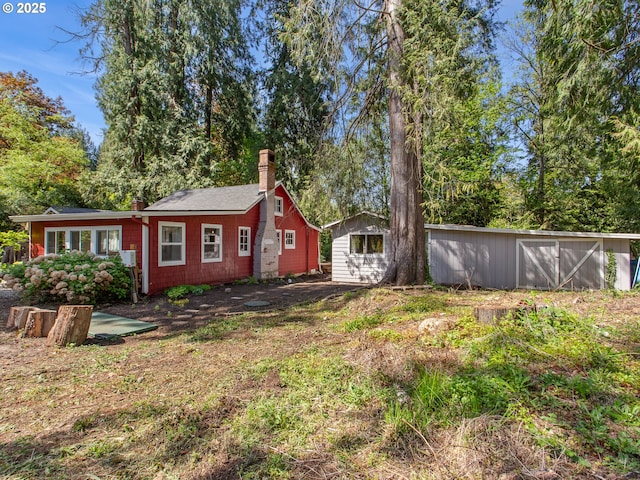 back of house featuring a chimney and an outdoor structure