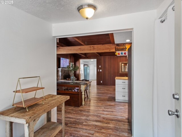 hallway featuring wood walls, wood finished floors, and beamed ceiling