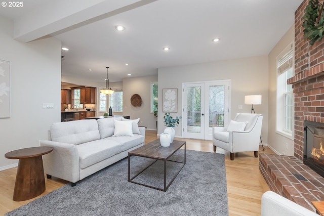 living room featuring recessed lighting, light wood-style flooring, a brick fireplace, and french doors